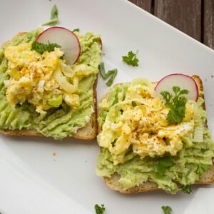 Deliciously prepared avocado and egg sandwiches garnished with radish on a white plate.