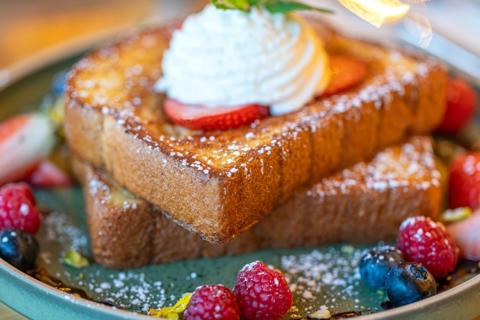 Close-up of French toast topped with whipped cream and berries, dusted with sugar.