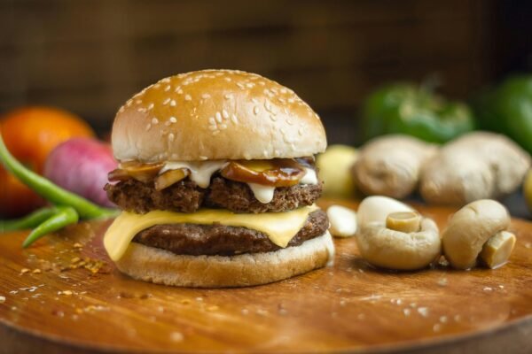Close-up of a gourmet burger with cheese, mushrooms, and vegetables on a wooden board.