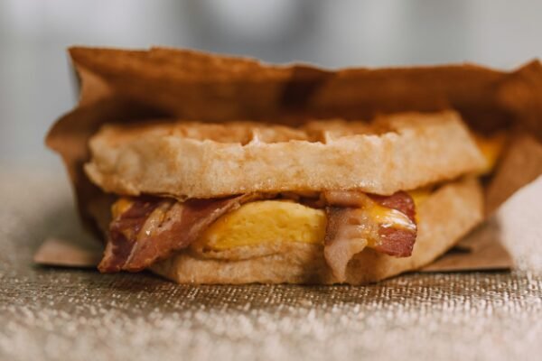 Mouthwatering waffle sandwich with bacon, egg, and cheese wrapped in paper.