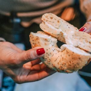 A delicious poppy seed bagel with cream cheese held by hands with red nails, perfect for food lovers.