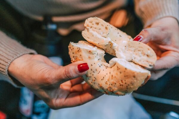 A delicious poppy seed bagel with cream cheese held by hands with red nails, perfect for food lovers.